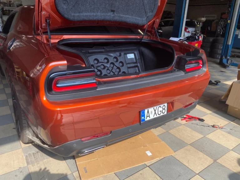 Tył pomarańczowego Dodge’a Challengera w warsztacie z otwartą klapą bagażnika