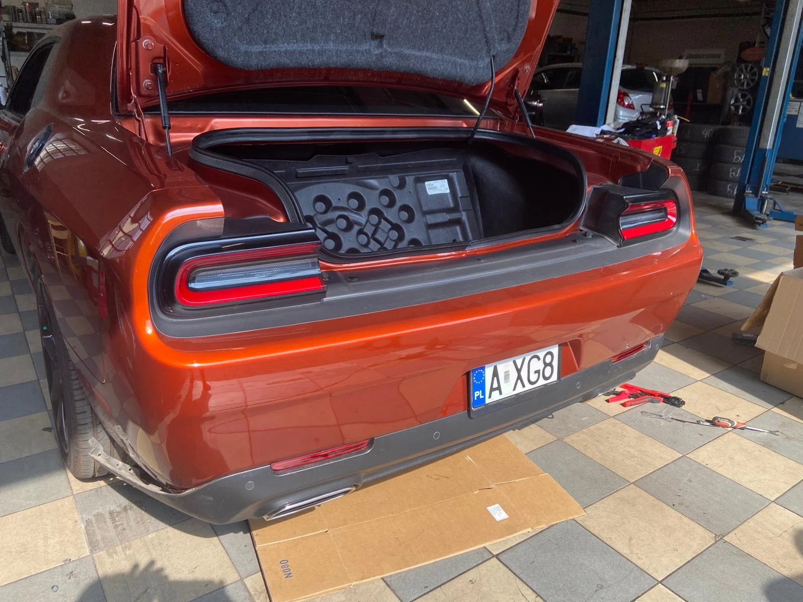 Tył pomarańczowego Dodge’a Challengera w warsztacie z otwartą klapą bagażnika